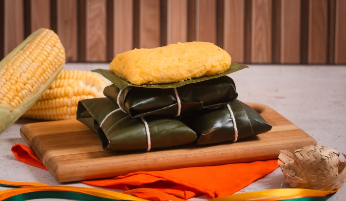 Pamonha de milho verde com erva-doce embrulhada em folhas de bananeira, corte cremoso sobre tábua