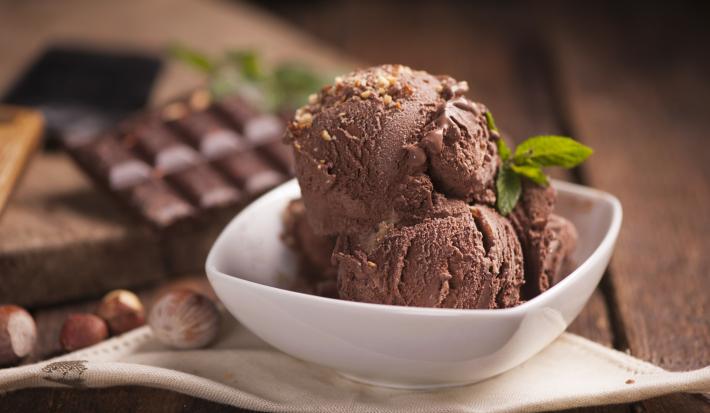 fotografia em tons de branco e marrom tirada de frente. Contém um recipiente quadrado branco com bolas de sorvete de chocolate.