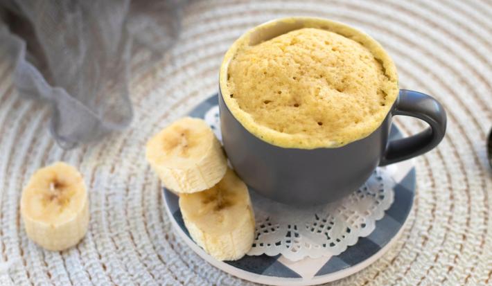 Imagem de um bolo de caneca com rodelas de banana ao lado.