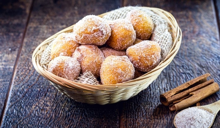 Em cima de uma mesa, cesta de palha com pano branco com bolinhos de chuva, polvilhado com açúcar de confeiteiro.