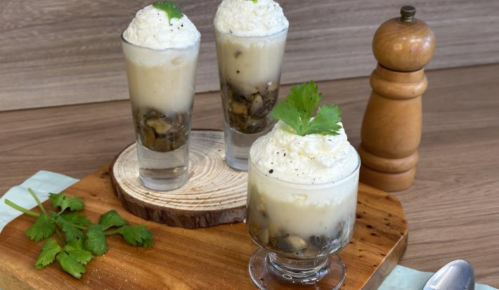 Fotografia em tons de marrom e verde com 3 taças ao centro. Dentro das taças existe um creme de cogumelos finalizados com chantilly no topo.