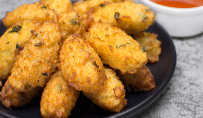 Fotografia de vários bolinhos de couve flor fritos em um prato de vidro preto.