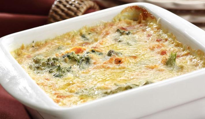 Fotografia em tons de vinho em uma bancada com uma toalha vinho, um recipiente branco retangular com os legumes gratinados dentro dele.