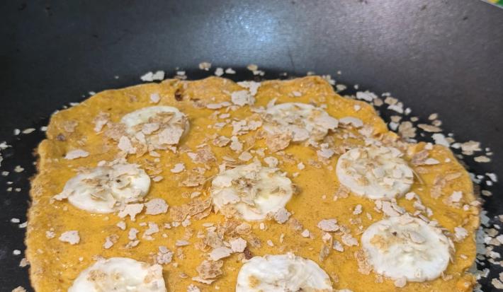 Fototgrafia de uma omelete de neston com rodelas de banana e neston cereias polvilhado, sobre uma frigideira.