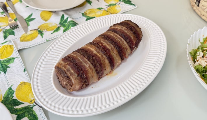 Foto vista de cima da receita de rocambole de carne com aveia, servido em um prato oval branco, bem dourado e assado, numa mesa de almoço