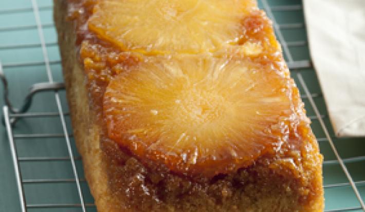 Foto em tons de azul e pardo, contém uma grade cinza com a torta com rodelas de abacaxi para decorar