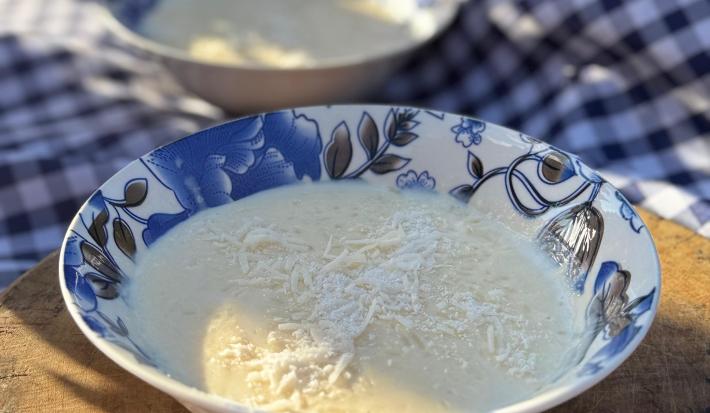 Fotografia em tons claros de dois recipientes fundo de cor azul, branco e preto com desenhos. Um deles está no centro da foto, o outro está no fundo sobre um pano quadriculado, preto e branco. Dentro dos recipientes tem arroz doce e coco.