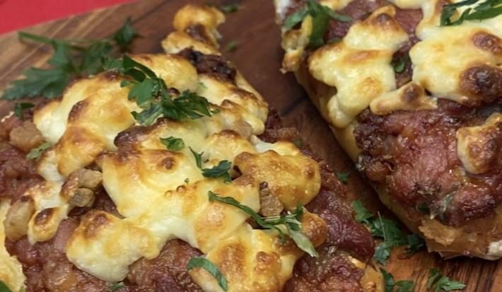Foto aproximada da receita de Pão com Linguiça feito na fritadeira elétrica. A receita está sobre uma tábua de madeira, com um pano em tom vermelho embaixo.