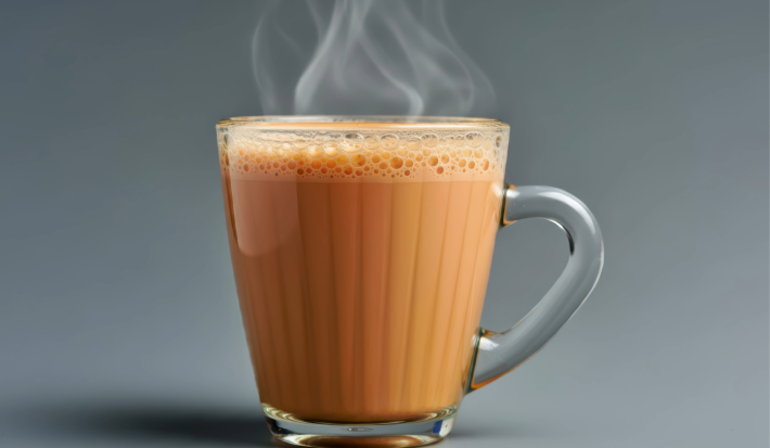 Caneca de vidro com bebida quente cremosa e vapor saindo da superfície, sobre fundo cinza.