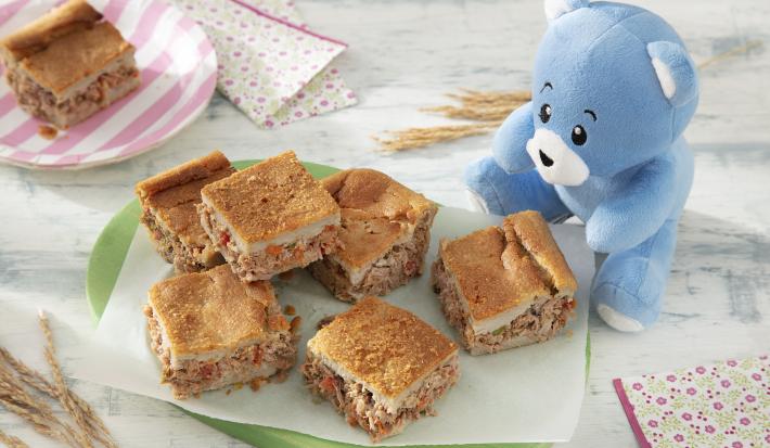 Foto da receita de Torta de Liquidificador. Observa-se um pratinho verde com 6 pedaços de torta de liquidificador sobrepostas em um papel manteiga. Ao lado direito, o ursinho Bo.