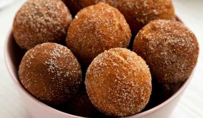 Em cima de uma mesa, tigela com bolinhos redondos, polvilhado com açúcar e canela.