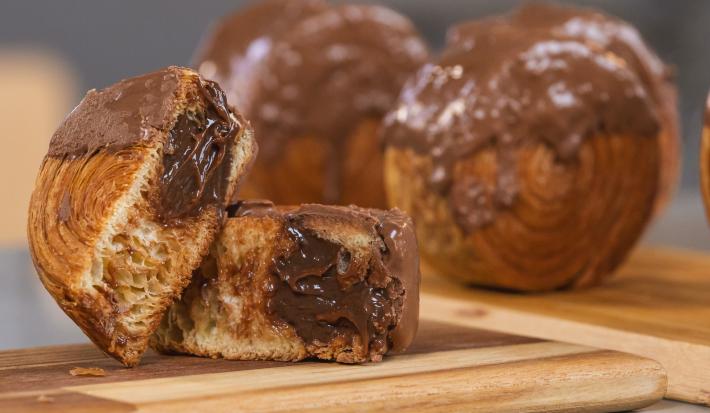 Imagem da receita de New York Rolls, servida sobre uma tábua de madeira, a da frente cortada ao meio mostrando o chocolate derretendo dentro e outros dois no fundo inteiros