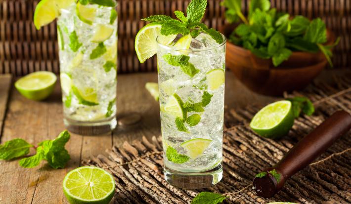 Foto da receita de Mojito Sem Álcool. Observa-se dois copos altos cheio de gelo e hortelã com a bebida dentro, decorado de limões.