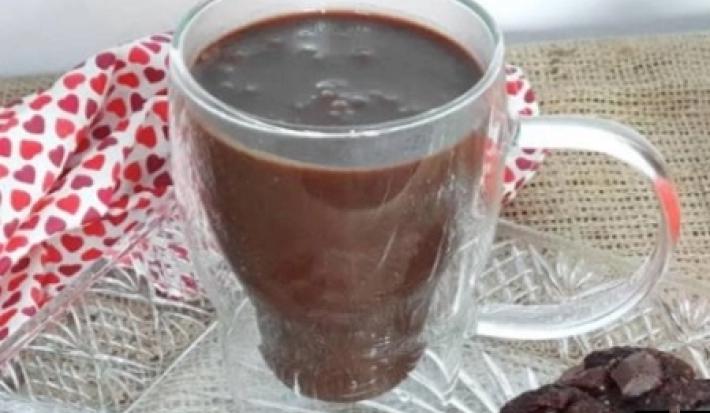 Foto da receita de Chocolate Quente. Observa-se uma xícara branca transparente com a bebida dentro, sobre um pires transparente de vidro.