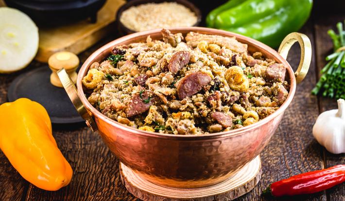 Receita de Feijão Tropeiro de Natal, tradicional e delicioso, feito com feijão, lombinho, bacon, linguiça calabresa e pimenta, servido em uma panela de cobre sobre uma mesa de madeira com diversos ingredientes in natura