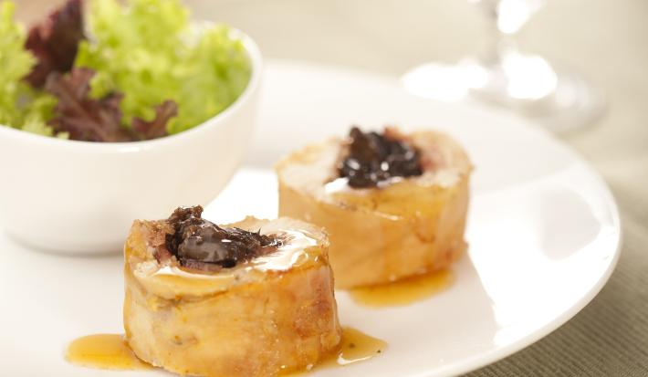 fotografia em tons de branco e bege de uma bancada bege vista de frente. Contém um prato redondo branco com duas fatias de rocambole e ao fundo um recipiente branco redondo com salada.