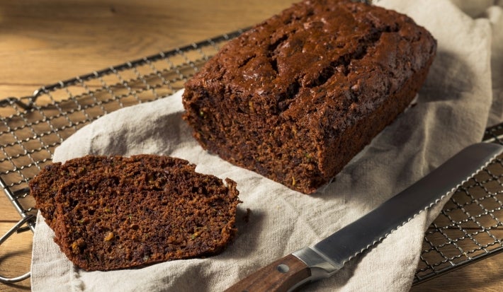 Em cima de uma mesa, grade com bolo de chocolate cortado em um fatia.