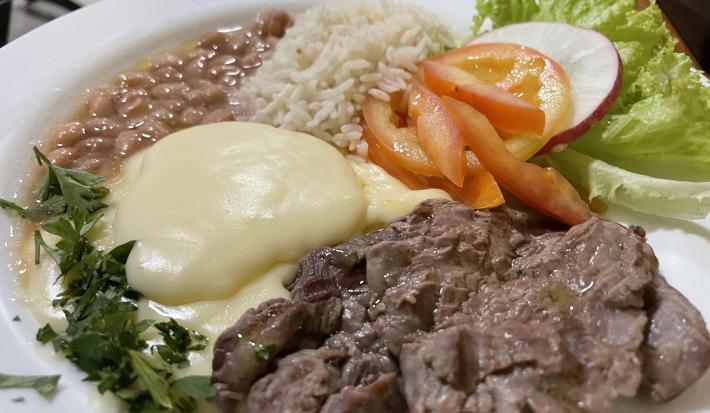 Foto da receita de Purê Francês. Observa-se um prato com um cremoso purê de batatas, acompanhado de arroz, feijão, iscas de carne e uma salada de tomate, rabanete e alface crespa.