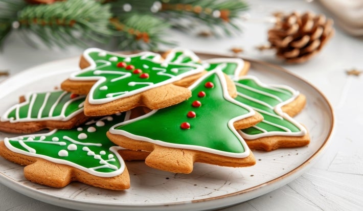 Em cima de uma mesa, prato redondo com biscoitos em formato de árvore de Natal, decorados com glacê verde e confeitos de bolinhas vermelhas.