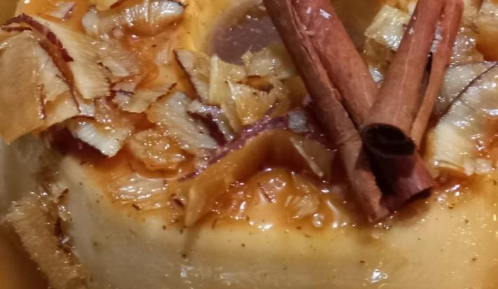 Fotografia de um pudim de cocada cremosa decorado com a calda com coco, lascas de coco e paus de canela.