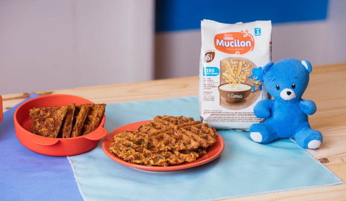 Fotografia em tons de azul em uma bancada de madeira e panos azuis, com um prato laranja e waffle em cima.