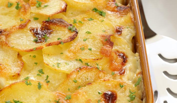 fotografia em tons de marrom e amarelo tirada de um recipiente marrom com batatas gratinadas dentro.