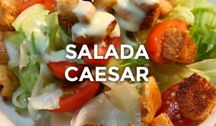 Foto da receita de Salada Caeser. Observa-se um prato com alface americana, tomates cereja, crouton, frango e molho