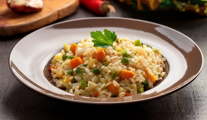 Em um prato redondo marrom, arroz cremoso com cenouras, ervilhas e frango desfiado.