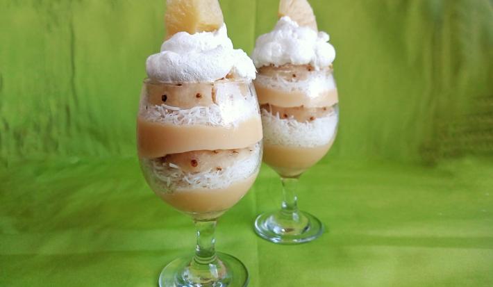 Fotografia em tons de verde com duas taças grandes de vidro ao centro. Dentro da taça existe um doce em camadas alternadas de abacaxi, coco ralado e chantilly