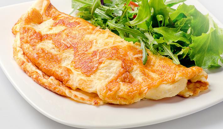 Foto aproximada de uma omelete dobrada ao meio e servida com algumas folhas verdes em um prato. Esta omelete foi prepara na airfryer de acordo com a receita.