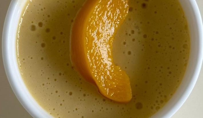 Fotografia em tons claros de três ramekins brancos sobre uma mesa branca. Dentro de cada ramekin tem uma receita de mousse de pêssego decorado com uma fatia da fruta.