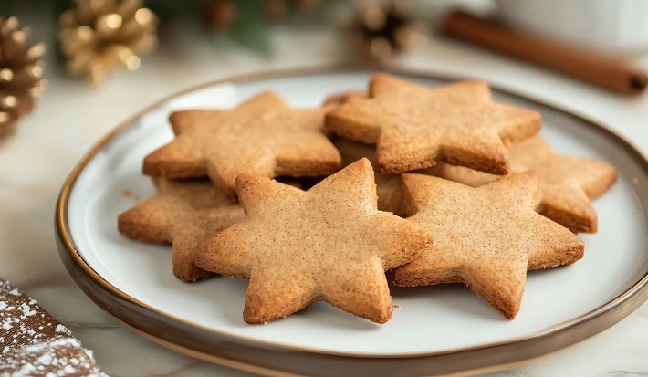 Em cima de uma mesa com enfeites de Natal, prato redondo com biscoitos em formato de estrelas.