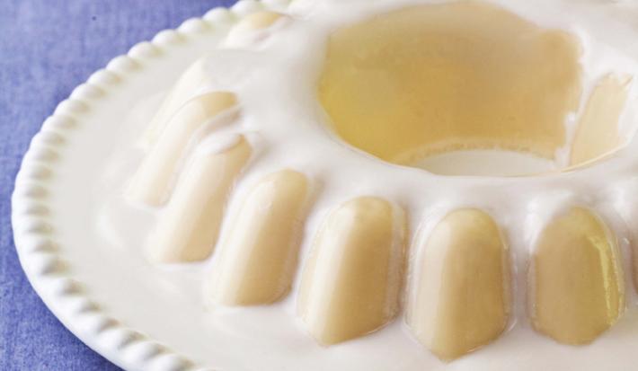 fotografia em tons de azul e branco de uma bancada azul vista de frente, contém um prato branco redondo com um flan e ao lado uma espátula para servir.