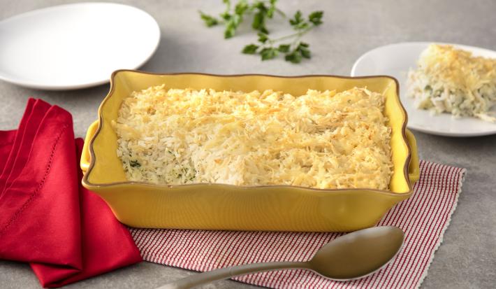 Fotografia em tons de amarelo e vermelho, ao centro está um refratário retangular com o arroz de forno. Abaixo está um guardanapo quadriculado vermelho e branco. Do lado esquerdo está um guardanapo vermelho e do outro uma colher de servir e um prato.