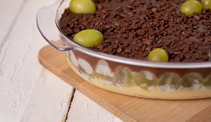 Imagem de creme branco com uvas verdes cortadas, ganache de chocolate, decorado com uvas inteiras e chocolate granulado.