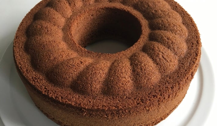 Em cima de uma mesa, prato branco redondo com bolo com furo no meio de chocolate fofinho.
