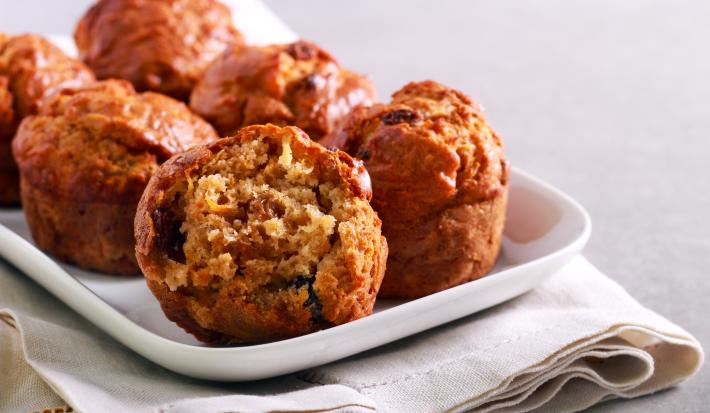 Fotografia de alguns muffins de maçã sobre um apoio retangular branco, o qual está apoiado em um paninho também branco. O pano está sobre uma bancada de cimento queimado claro.