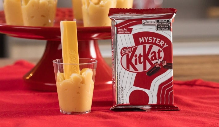 Fotografia em tons de vermelho com um prato vermelho ao centro. Em cima do prato existe uma receita de brigadeiro de maracujá de colher com vários kitkats mysterys espetados como decoração. Fotografia em tons de vermelho com um prato vermelho ao centro. Em cima do prato existe uma receita de brigadeiro de maracujá de colher com vários kitkats mysterys espetados como decoração.