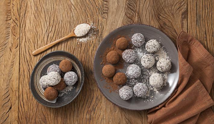 fotografia em tons de marrom e branco de uma bancada marrom vista de cima, contém dois pratos redondos cinza e ambos contém trufas com aveia por cima e chocolate