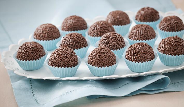 Foto de um prato branco que está em cima de um pano azul com vários brigadeiros dentro de forminhas azuis