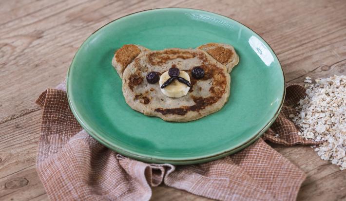 Foto da receita de Panqueca de Banana. Observa-se um pratinho verde e a panquequinha com cara de ursinho.