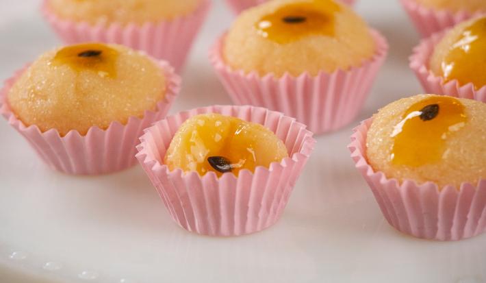 Fotografia em tons de rosa com várias forminhas de brigadeiro ao centro. Dentro de cada forminha existe brigadeiros feitos de maracujá finalizados com geleia de maracujá no topo.