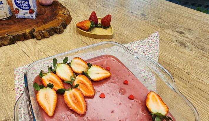 Foto da receita de Doce amor de morango. Observa-se uma travessa com o creme rosa e morangos frescos decorando.