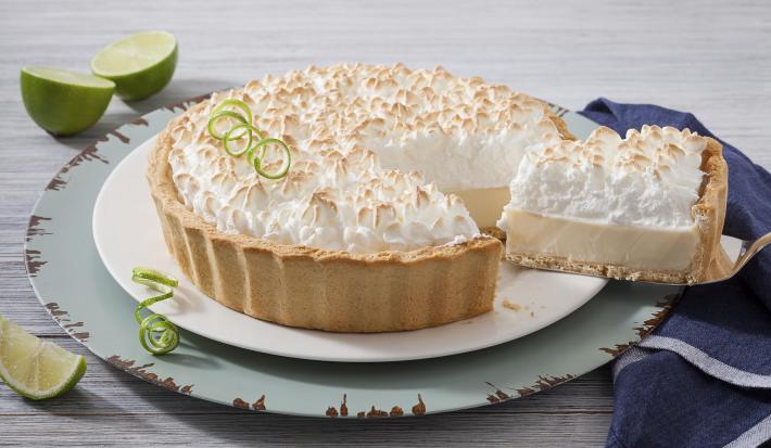 Imagem de uma torta de limão com merengue em um prato branco e uma fatia sendo retirado por uma espátula.