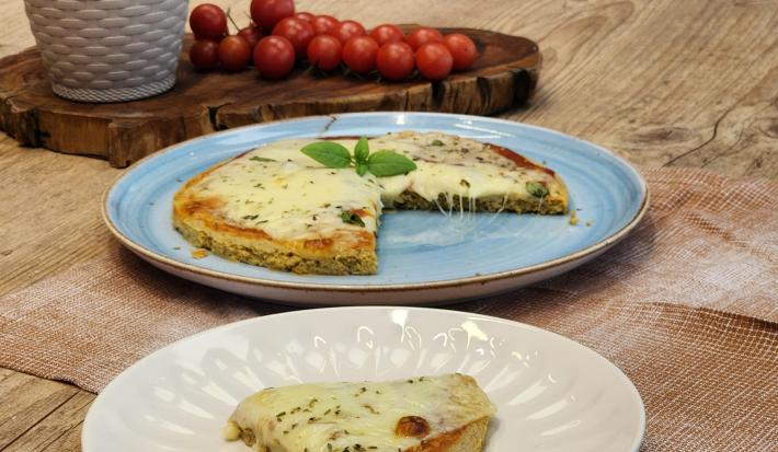 Fotografia em tons de marrom com um prato azul ao centro. Em cima do prato existe uma pizza com massa de Aveia coberta com queijo muçarela e orégano.