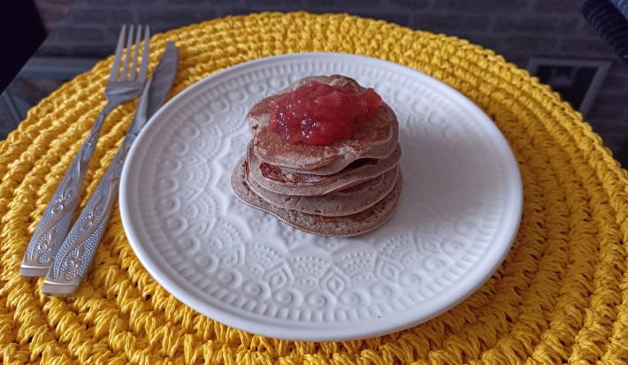 Imagem da receita de Panqueca de batata doce sem glúten com cobertura de geleia de frutas, em um prato branco, sobre uma mesa e ao lado os talheres