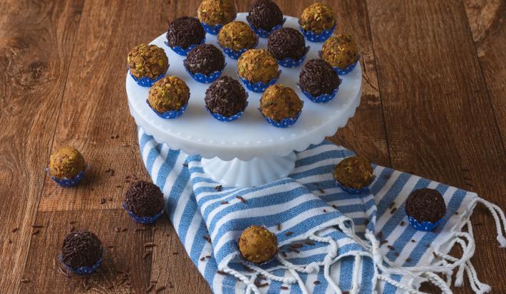 Foto da receita de brigadeiro de pistache da agatha souza, servido em forminhas azuis, sobre um prato em um bancada de madeira com um tecido azul listrado