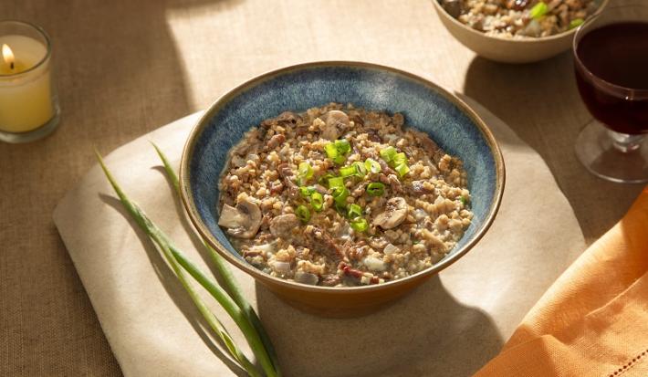 Foto em tons de marrom da receita de risoto de filé mignon e gorgonzola servida em um bowl de cerâmica azul sore um pano bege com ramos de alho poró ao lado