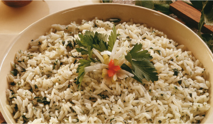 fotografia em tons de bege tirada de uma panela redonda bege com alças, que contém arroz e ervas dentro.
