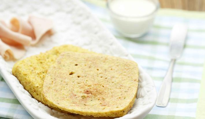em um recipiente branco contém duas fatias de pão, abaixo dois panos nas cores verde e branco e ao lado uma xícara de leite e um garfo.